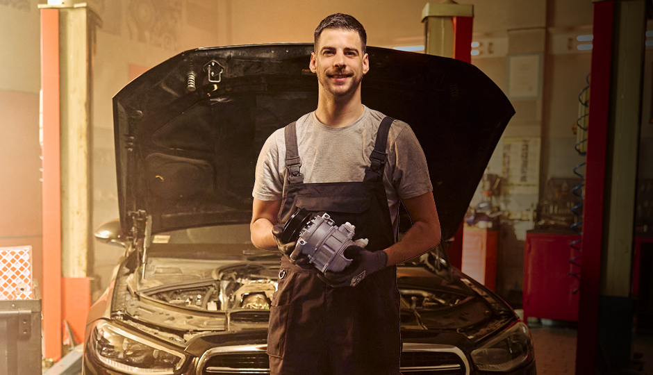 Mechanic holding air compressor in front of an opened bonnet